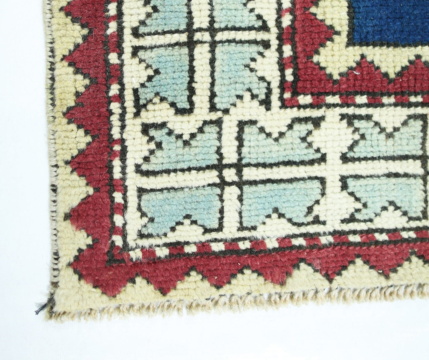 A corner view of a vintage Turkish rug featuring a geometric pattern in blue, red, and cream.