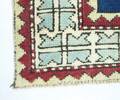 A corner view of a vintage Turkish rug featuring a geometric pattern in blue, red, and cream.