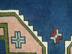 A close-up of a vintage Turkish rug featuring geometric cross motifs in blue, pink, and green.