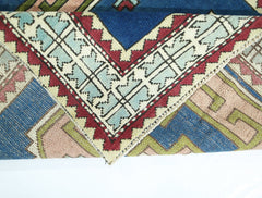 A corner of a vintage handmade Turkish wool rug featuring geometric patterns in blue, red, and tan.