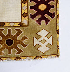 A corner view of a vintage Turkish Milas rug featuring geometric floral motifs in olive, cream, and maroon.