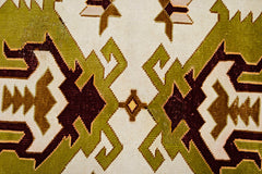 A close-up of a vintage Turkish Milas rug featuring geometric patterns in olive, brown, and cream.