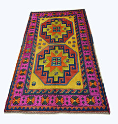 A rectangular vintage Turkish rug featuring two large geometric medallions in orange and green on a yellow field with a vibrant pink border.