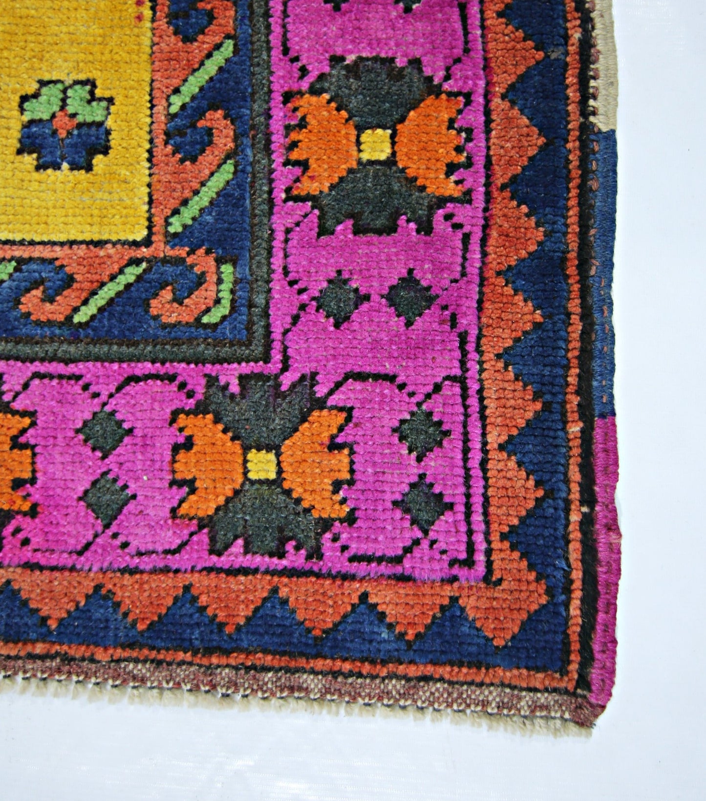 A corner view of a vintage handmade Turkish wool rug featuring vibrant pink, orange, and blue patterns.