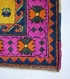 A corner view of a vintage handmade Turkish wool rug featuring vibrant pink, orange, and blue patterns.