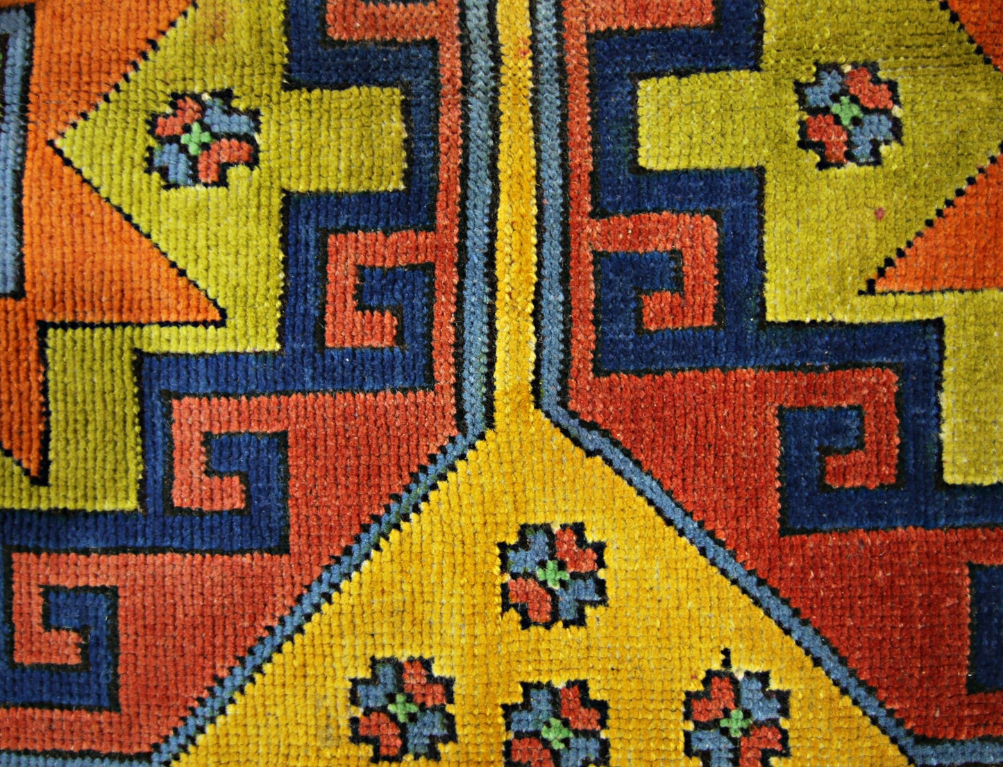 A close-up of a vintage Turkish rug featuring geometric patterns in vibrant yellow, red, and blue.