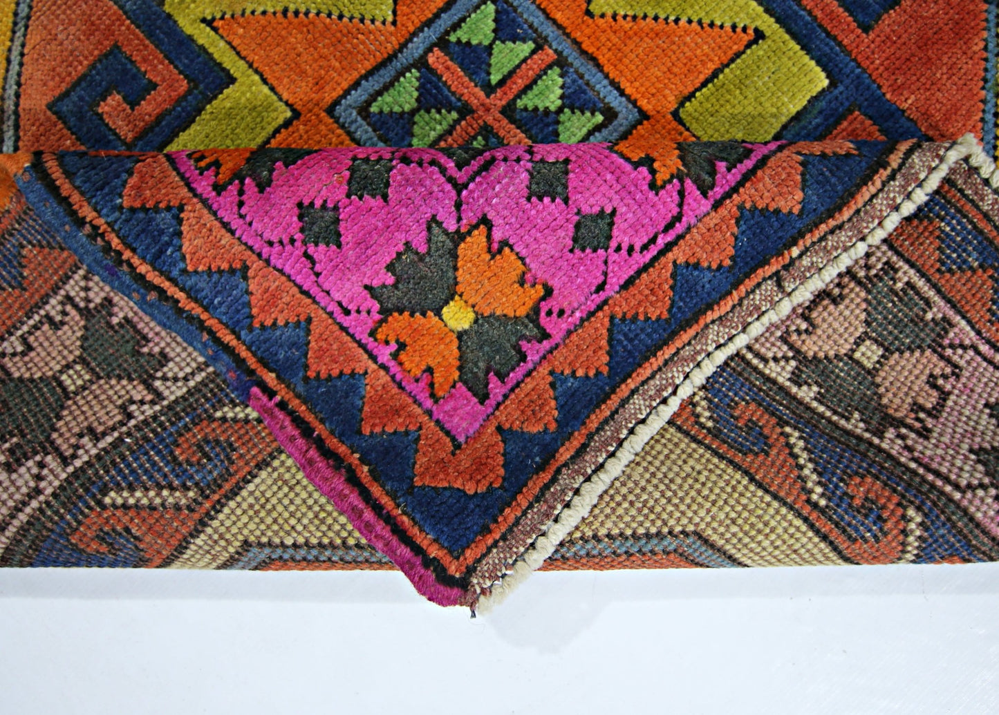 A folded vintage Turkish rug featuring a vibrant geometric pattern in pink, orange, and blue.