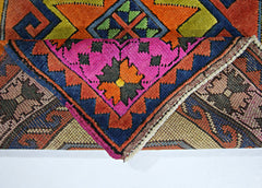 A folded vintage Turkish rug featuring a vibrant geometric pattern in pink, orange, and blue.