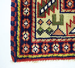 A corner view of a vintage handmade Turkish rug featuring geometric patterns in red, blue, and cream.