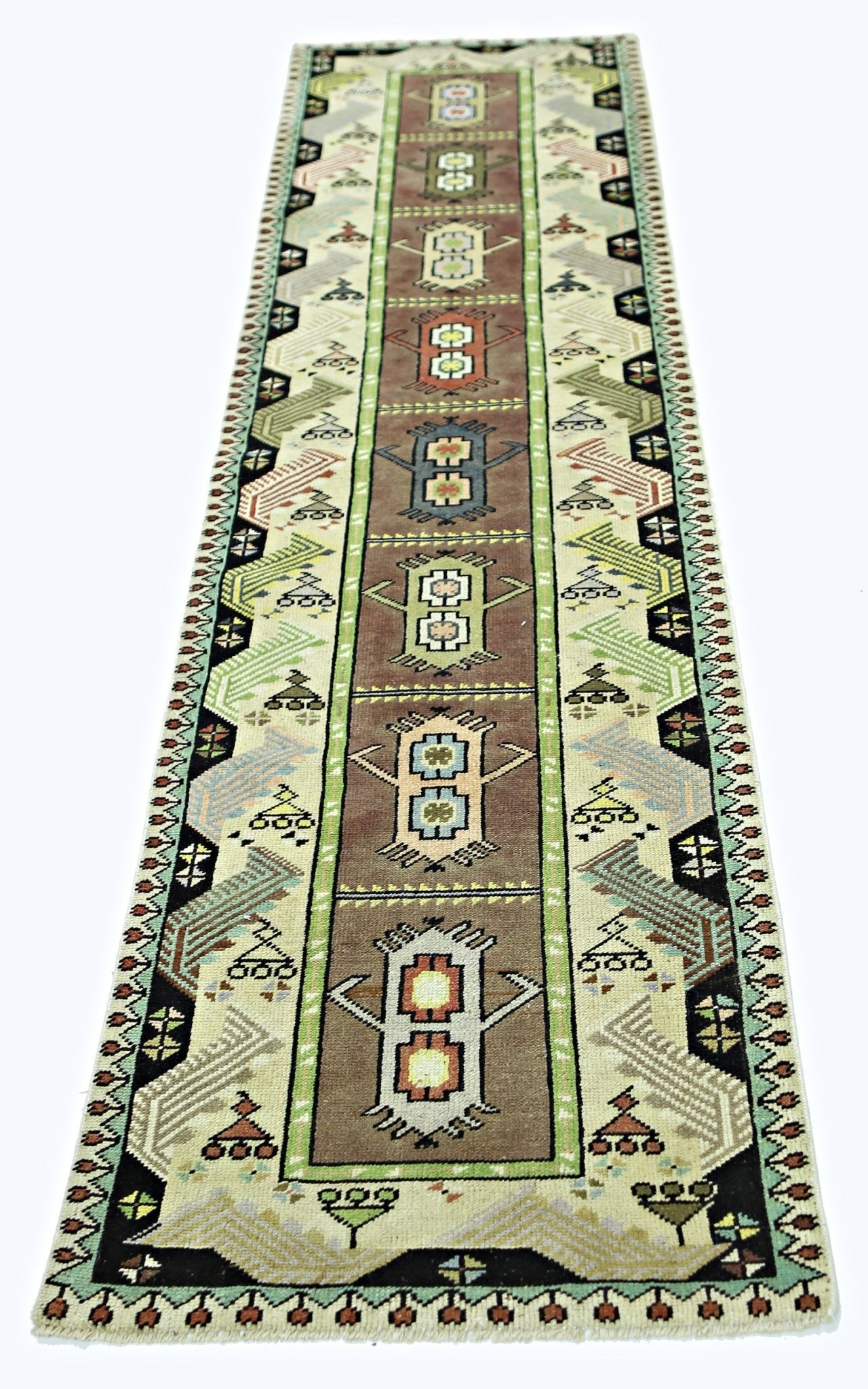 A vintage handmade Turkish runner rug featuring geometric motifs in brown, green, and cream tones.