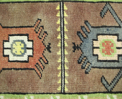 A close-up of a vintage Turkish runner featuring geometric motifs in brown, orange, and blue wool.