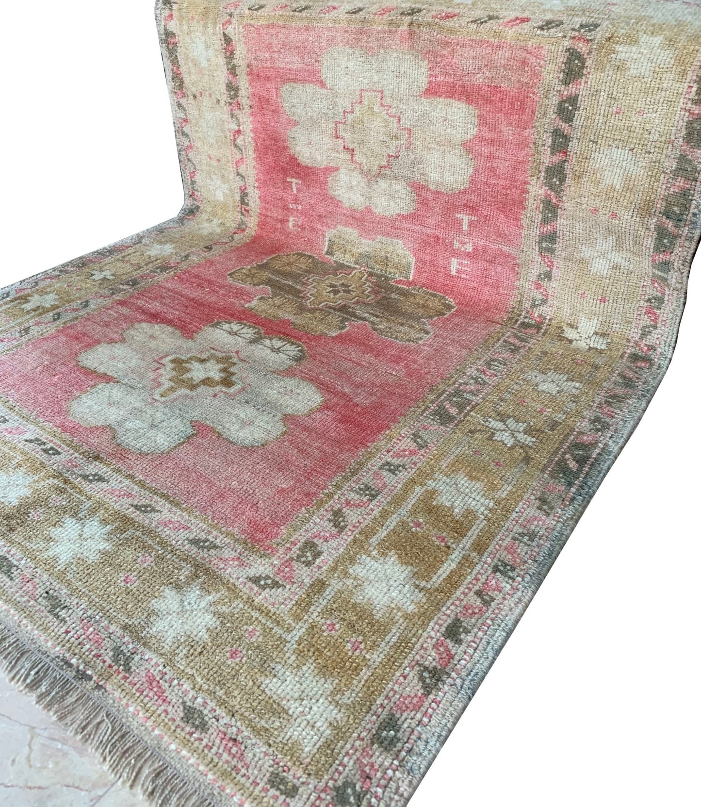 A vintage Turkish Oushak rug featuring a pink field with tribal floral motifs and woven initials.