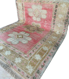 A vintage Turkish Oushak rug featuring a pink field with tribal floral motifs and woven initials.