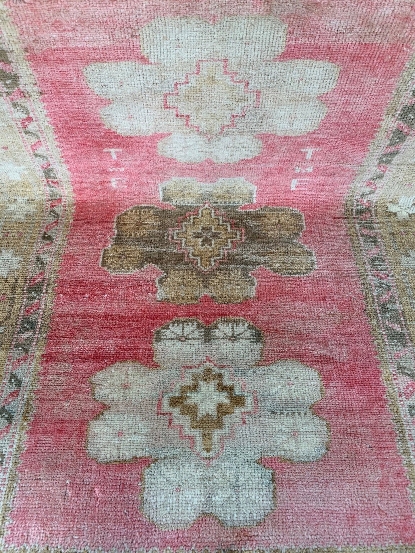 A vintage Turkish Oushak rug featuring a pink field with tribal floral motifs and woven initials.