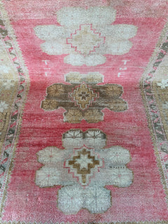 A vintage Turkish Oushak rug featuring a pink field with tribal floral motifs and woven initials.