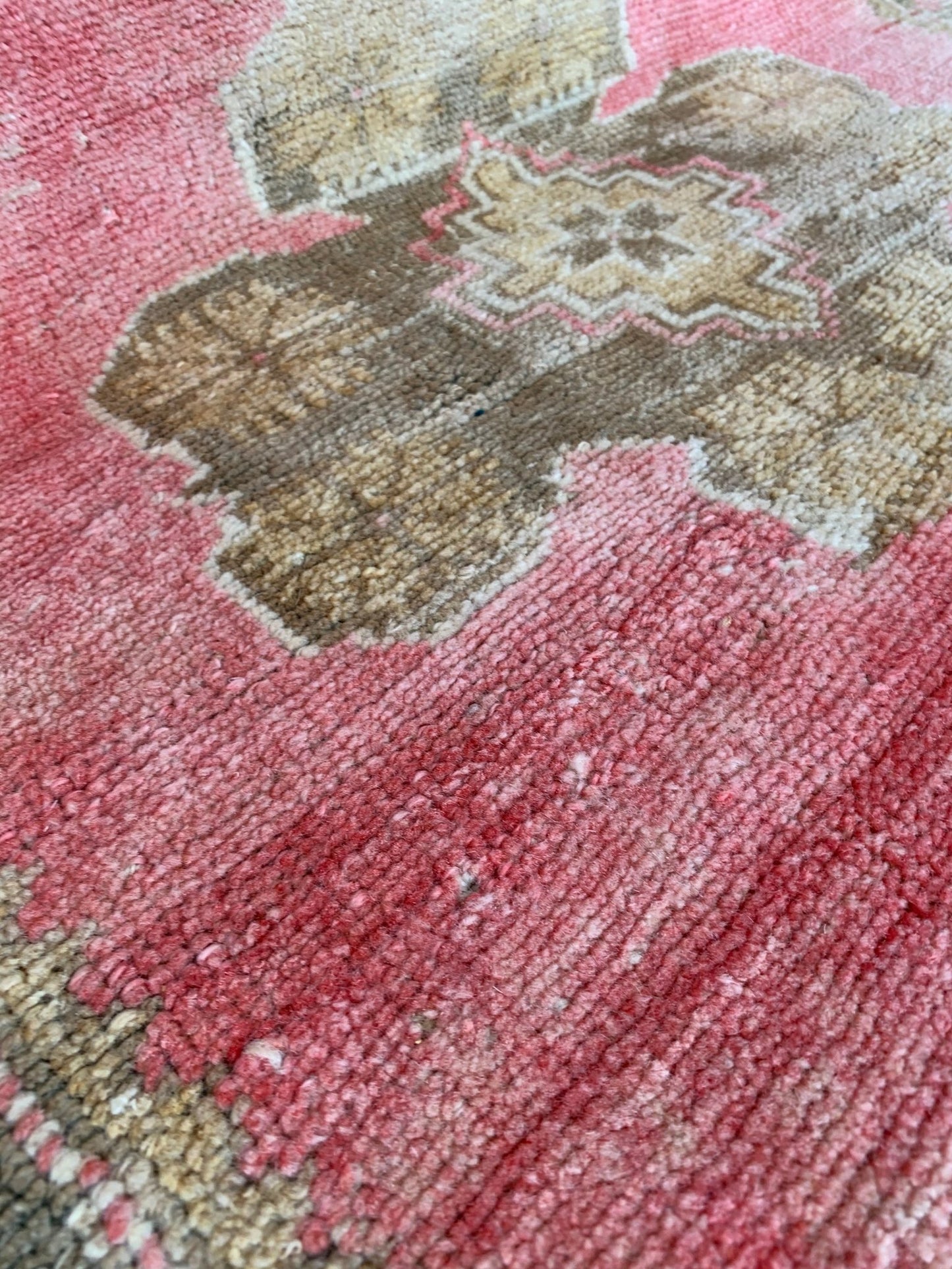 A close-up of a vintage Turkish Oushak rug featuring a tribal floral pattern in pink and tan.
