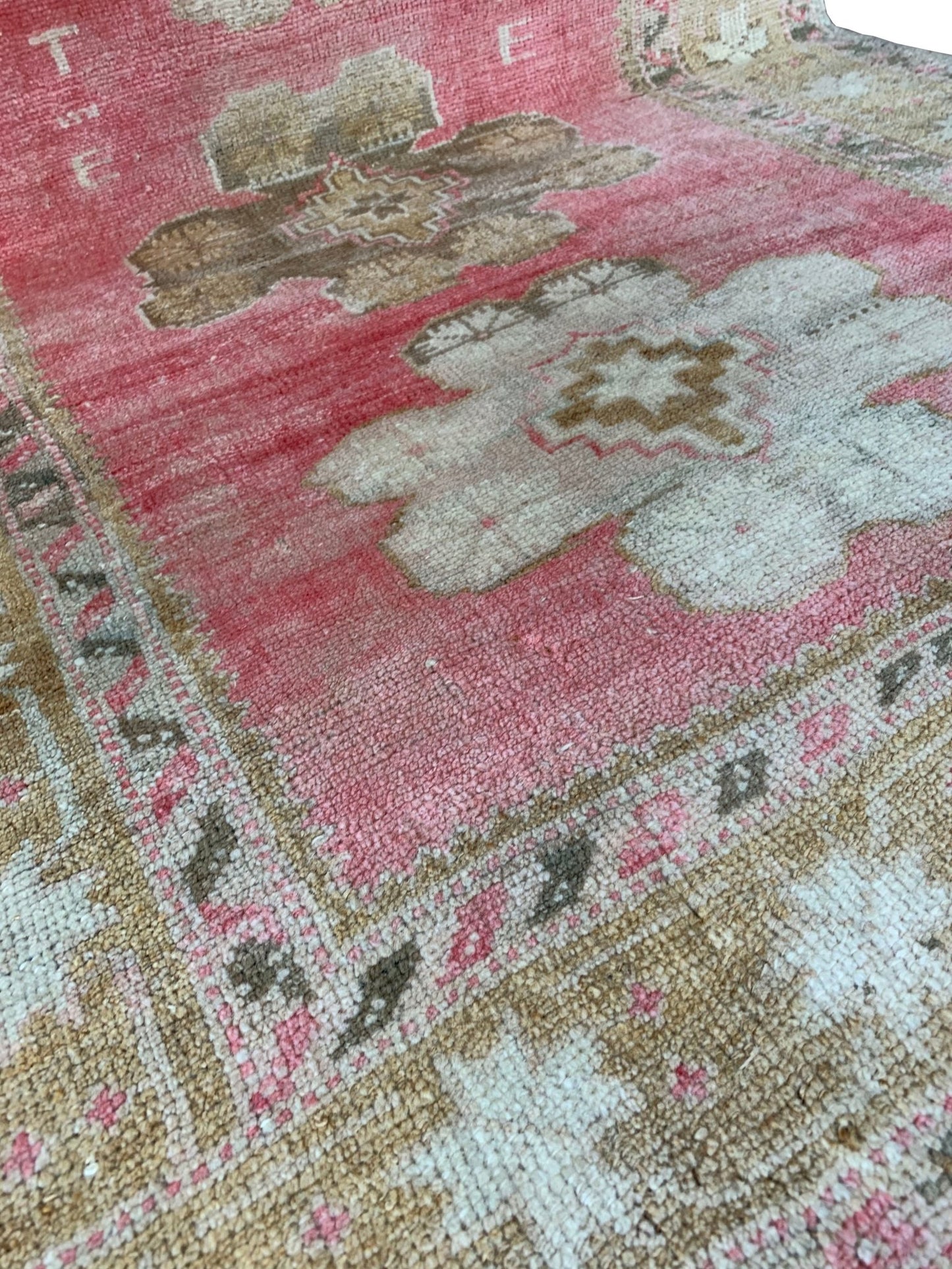 A vintage Turkish Oushak rug featuring a pink field with tribal floral motifs and woven initials.