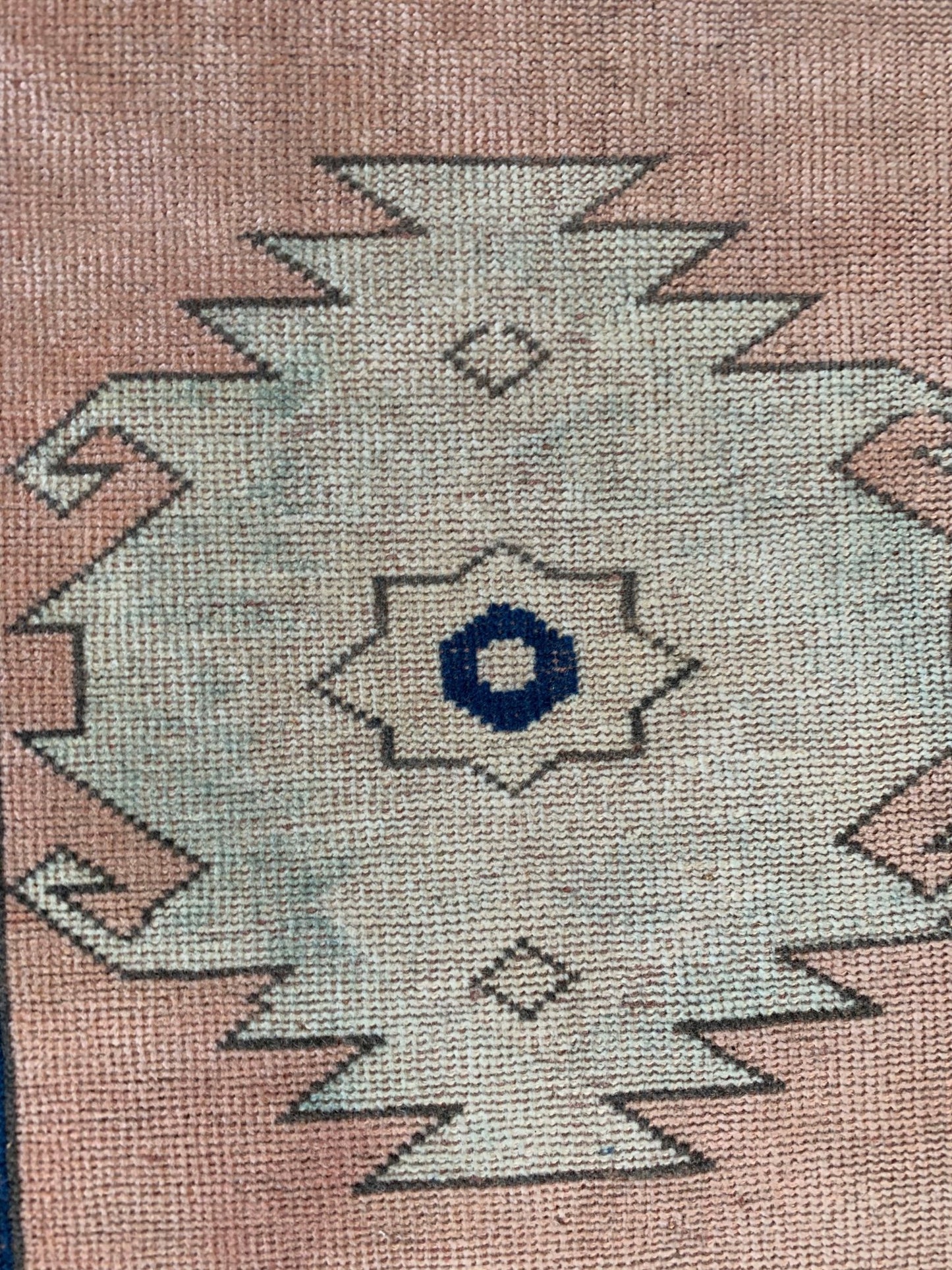 A vintage Turkish Oushak runner featuring a central tribal medallion on a soft pink background.