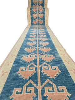 A long vintage Turkish Oushak runner featuring pink tribal motifs on a blue field.