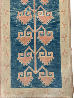 A vintage Turkish Oushak runner featuring pink geometric tribal motifs on a blue field.