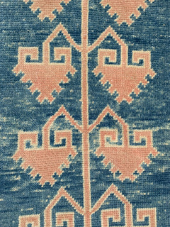 A vintage Turkish Oushak runner featuring pink geometric Seljuk motifs on a blue wool background.