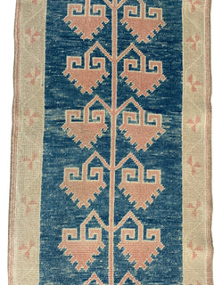 A vintage Turkish Oushak runner featuring pink geometric tribal motifs on a blue field.
