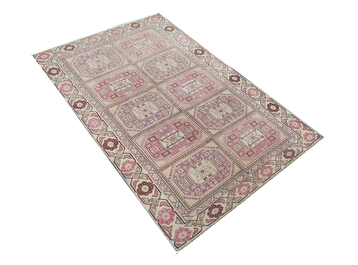 A vintage handmade Turkish wool rug featuring a repeating geometric medallion pattern in pink and tan.