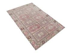 A vintage handmade Turkish wool rug featuring a repeating geometric medallion pattern in pink and tan.