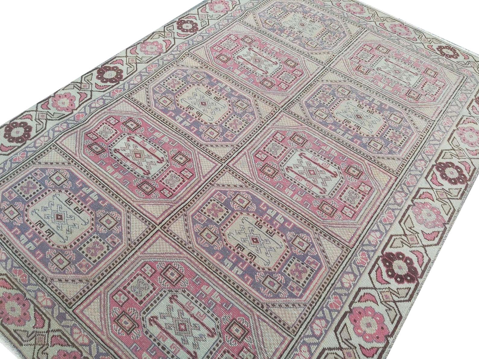 A vintage Turkish rug featuring a geometric grid pattern in shades of pink, purple, and cream.