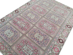 A vintage Turkish rug featuring a geometric grid pattern in shades of pink, purple, and cream.