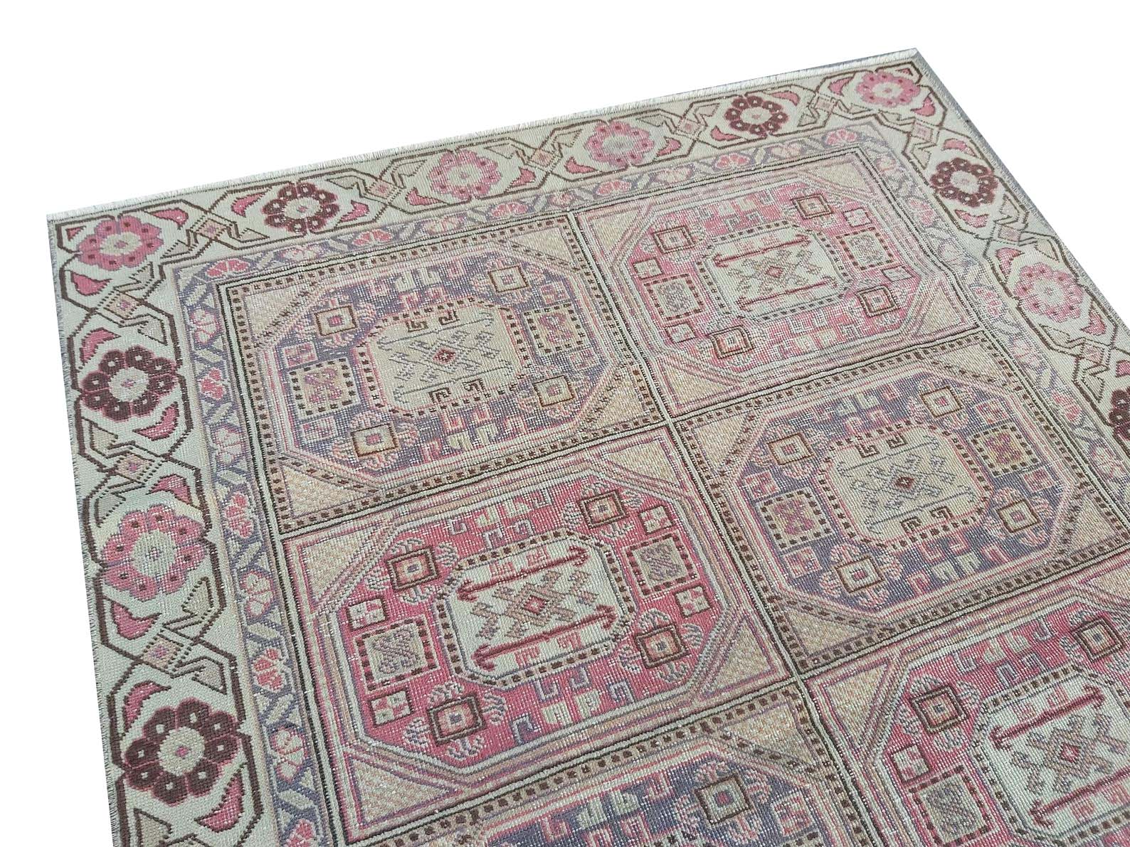 A vintage handmade Turkish wool rug featuring a geometric pattern in shades of pink and purple.