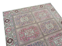 A vintage handmade Turkish wool rug featuring a geometric pattern in shades of pink and purple.