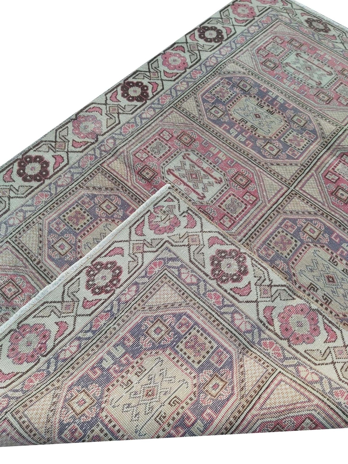 A vintage handmade Turkish wool rug featuring geometric patterns in pink, purple, and cream.