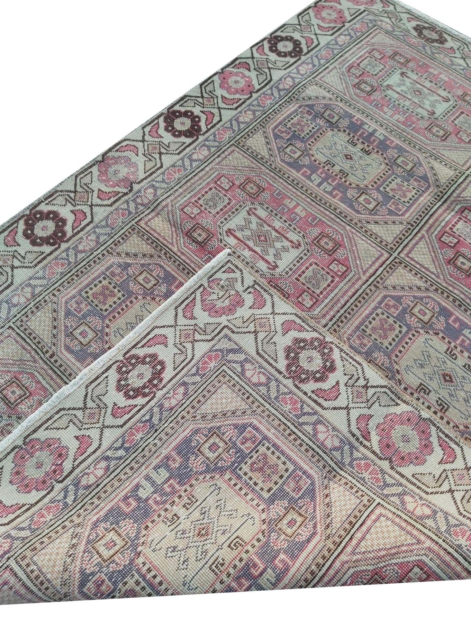 A vintage handmade Turkish wool rug featuring geometric patterns in pink, purple, and cream.