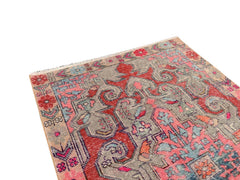 A handmade vintage Turkish rug featuring a geometric floral pattern in red, pink, and grey tones.