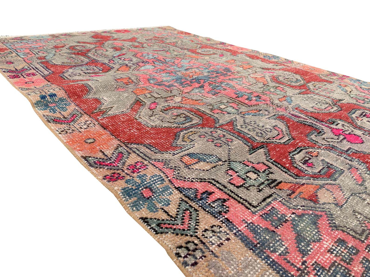 A vintage handmade Turkish wool rug featuring a distressed floral pattern in red, blue, and pink.