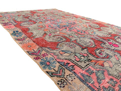 A vintage handmade Turkish wool rug featuring a distressed floral pattern in red, blue, and pink.