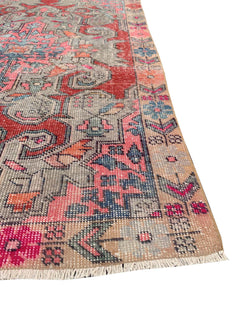 A handmade vintage Turkish wool rug featuring a geometric pattern in red, blue, and pink tones.