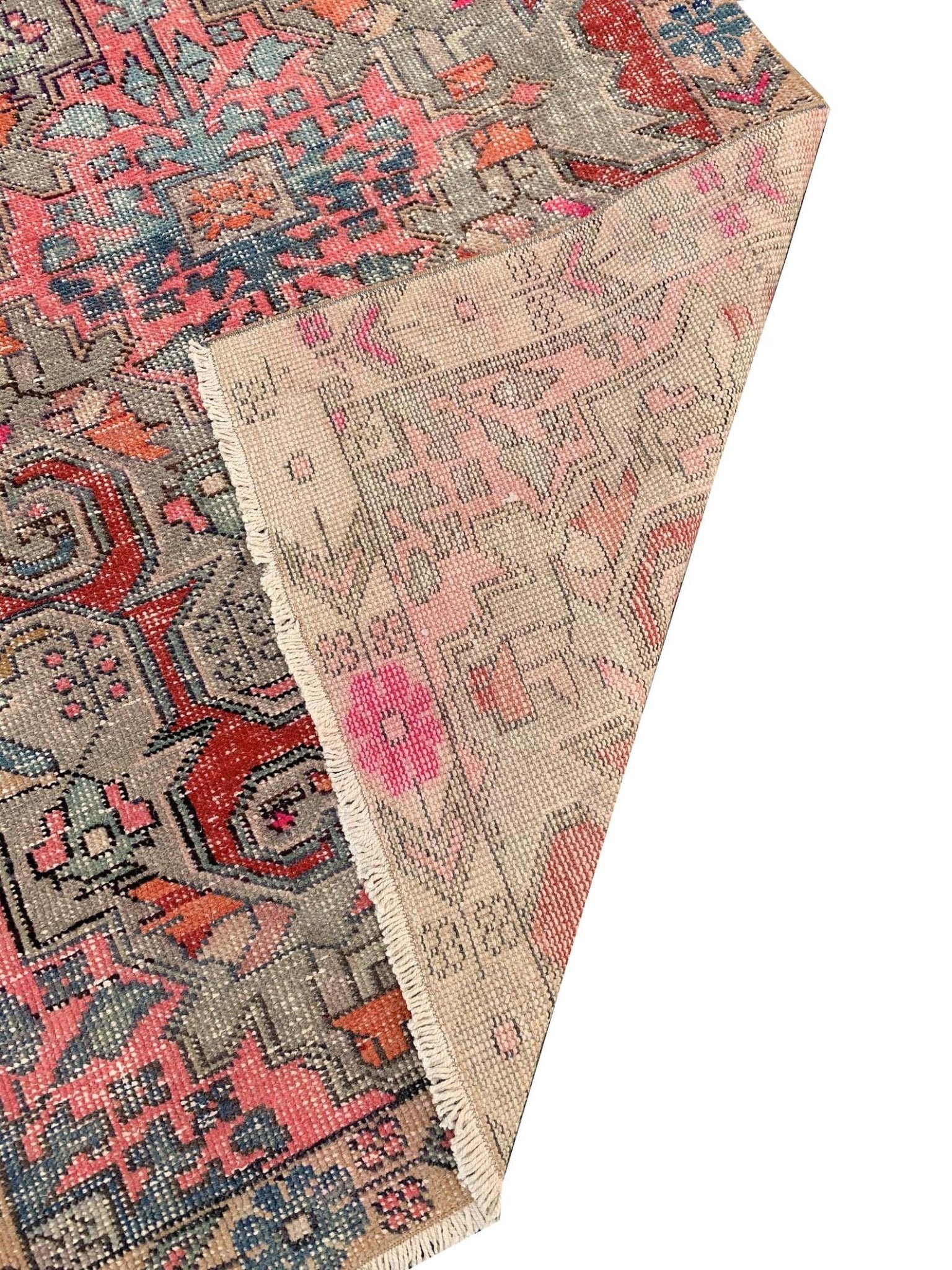A vintage handmade Turkish wool rug featuring a geometric pattern in pink, red, and grey tones.