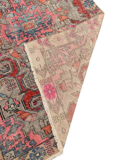 A vintage handmade Turkish wool rug featuring a geometric pattern in pink, red, and grey tones.