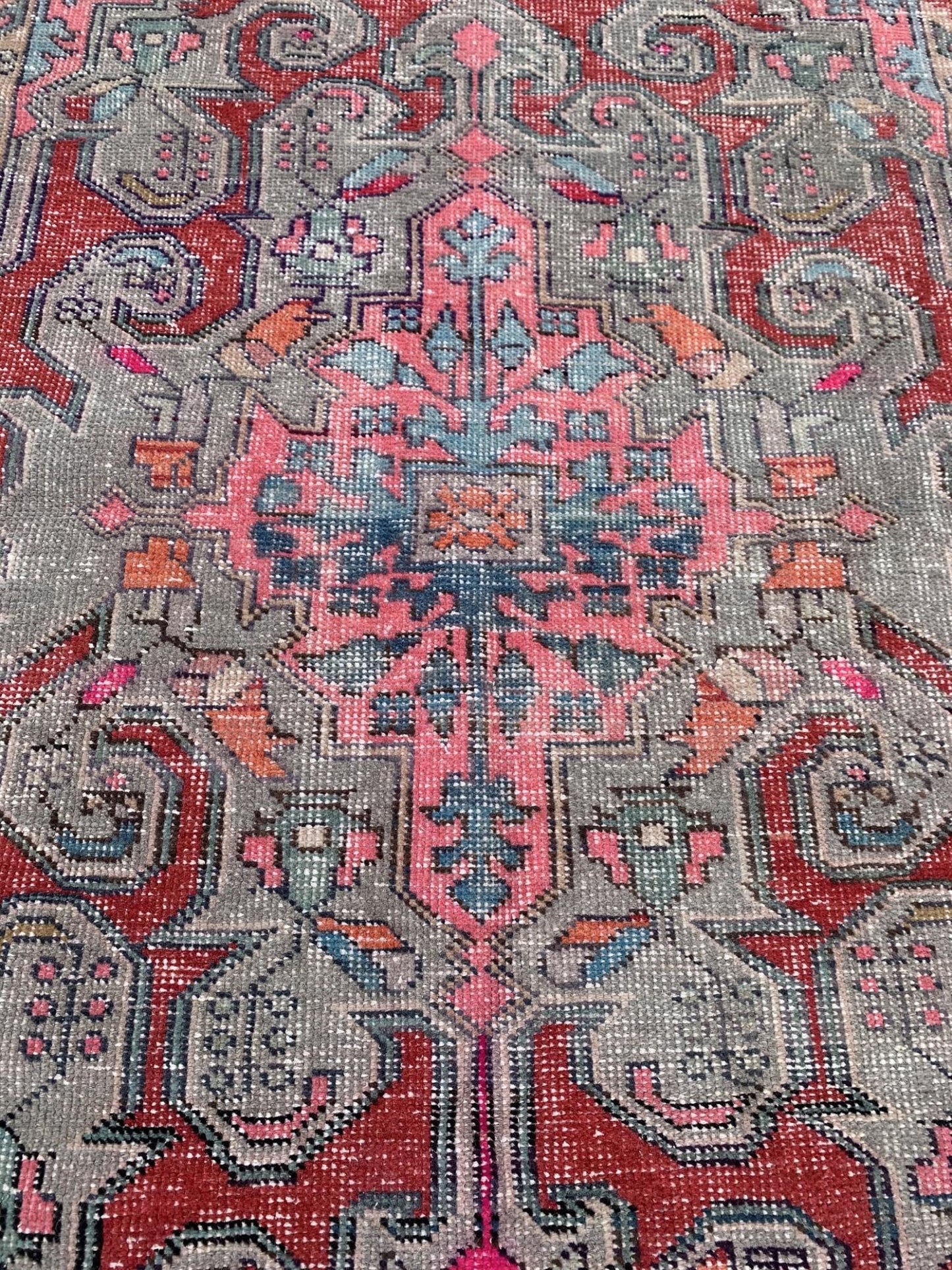 A vintage handmade Turkish wool rug featuring a geometric floral pattern in red, pink, and grey.