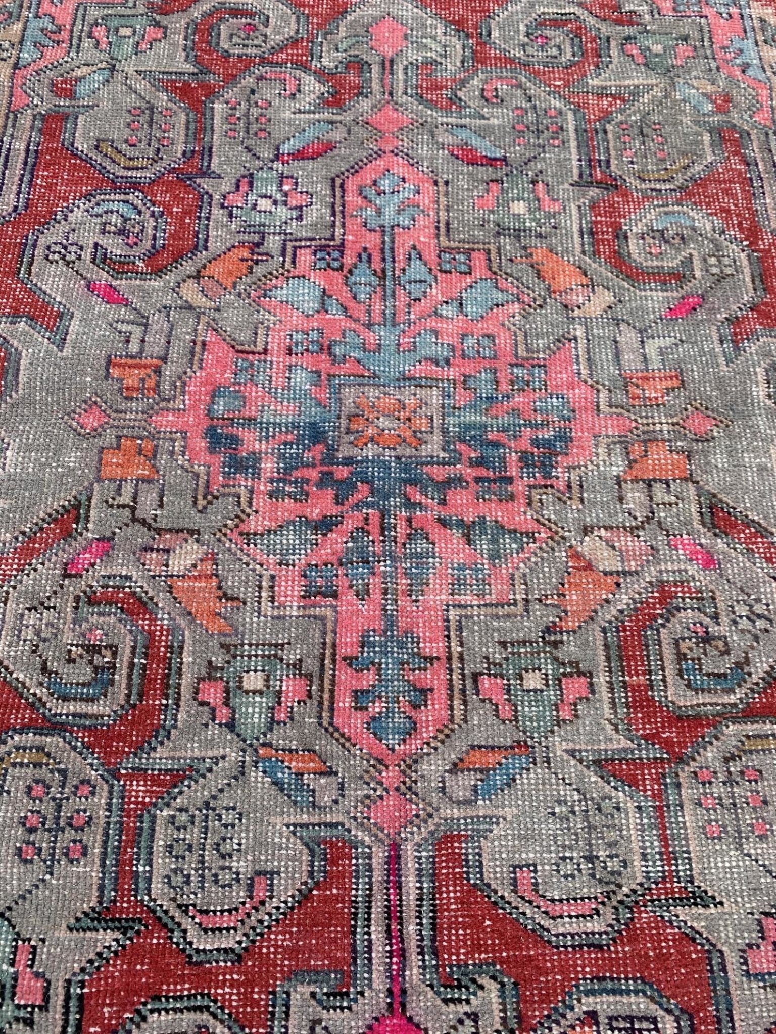 A vintage handmade Turkish wool rug featuring a geometric floral pattern in red, pink, and grey.
