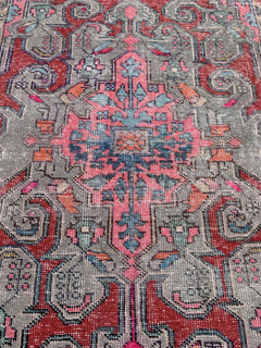 A vintage handmade Turkish wool rug featuring a geometric floral pattern in red, pink, and grey.