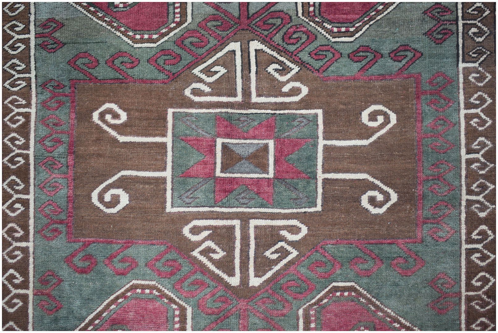A vintage handwoven Turkish rug featuring a geometric brown, green, and red pattern.