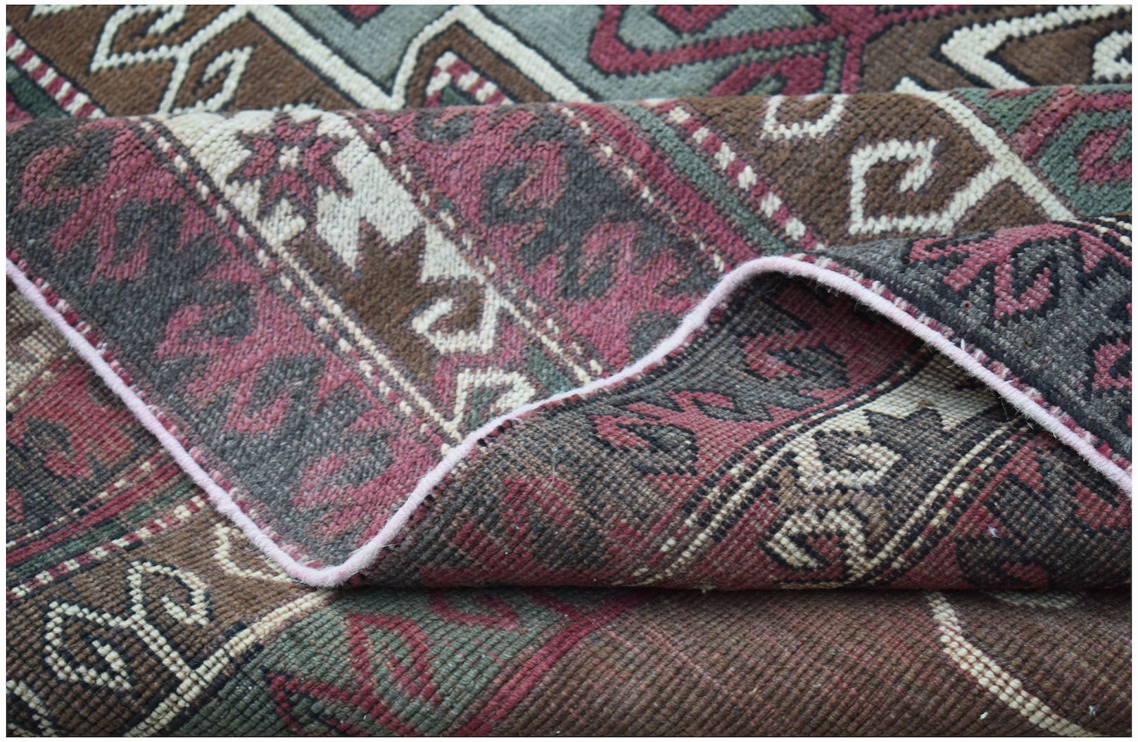 A folded vintage Turkish rug featuring intricate geometric patterns in muted red, brown, and green.