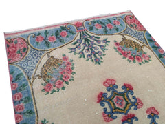 A vintage handmade Turkish wool rug featuring a floral pattern on a cream background.