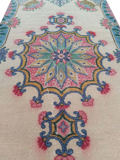 A vintage handmade Turkish wool rug featuring a central floral medallion on a cream background.