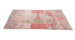 A rectangular vintage Turkish rug featuring a faded red and pink geometric pattern.