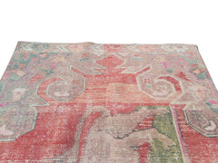 A vintage handmade Turkish wool rug featuring a faded geometric pattern in red and muted tones.