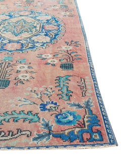 A vintage handmade Turkish rug featuring a pink field with blue floral motifs and a central medallion.
